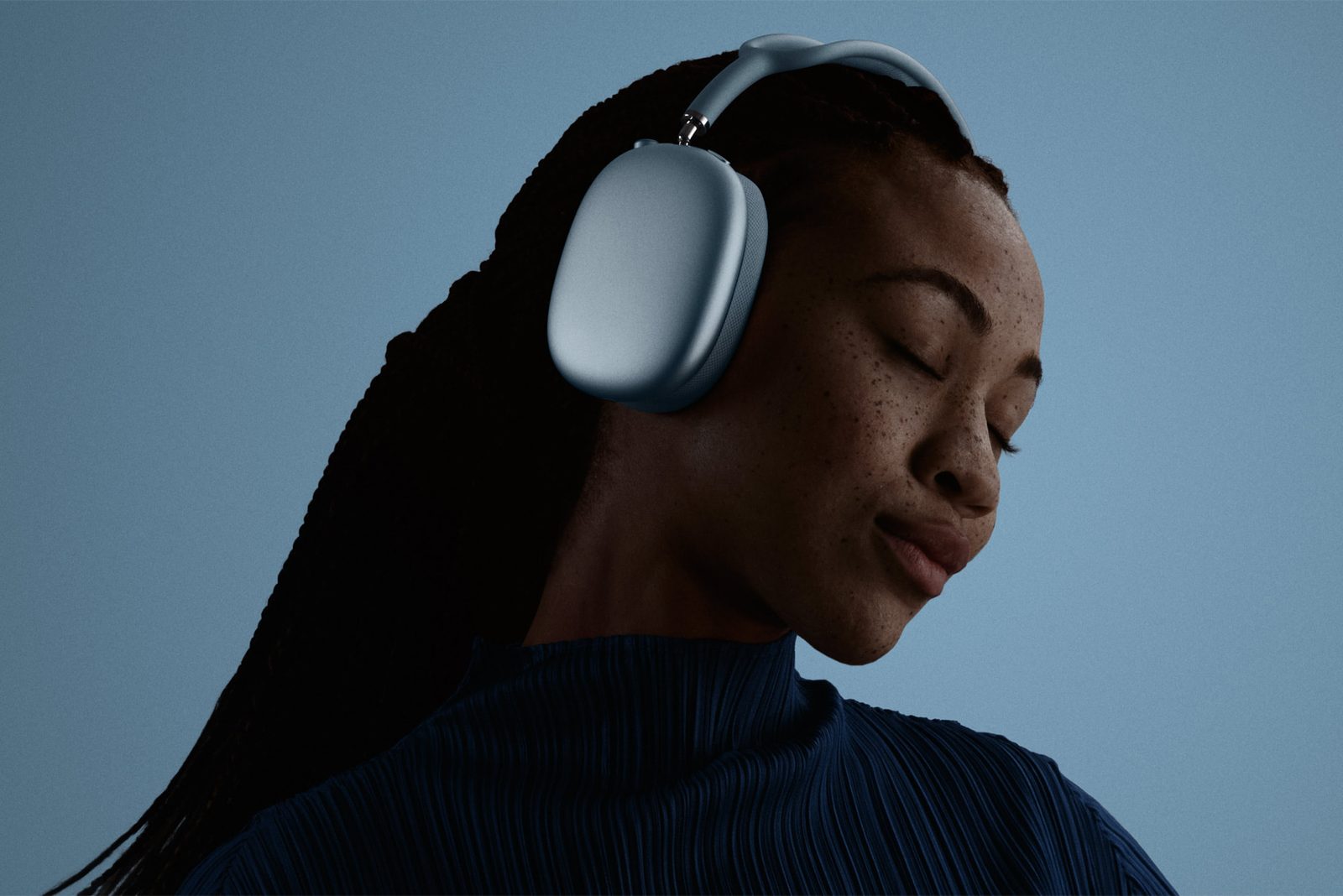 Person med slutna ögon bär blå AirPods Max 2 mot en blå bakgrund.