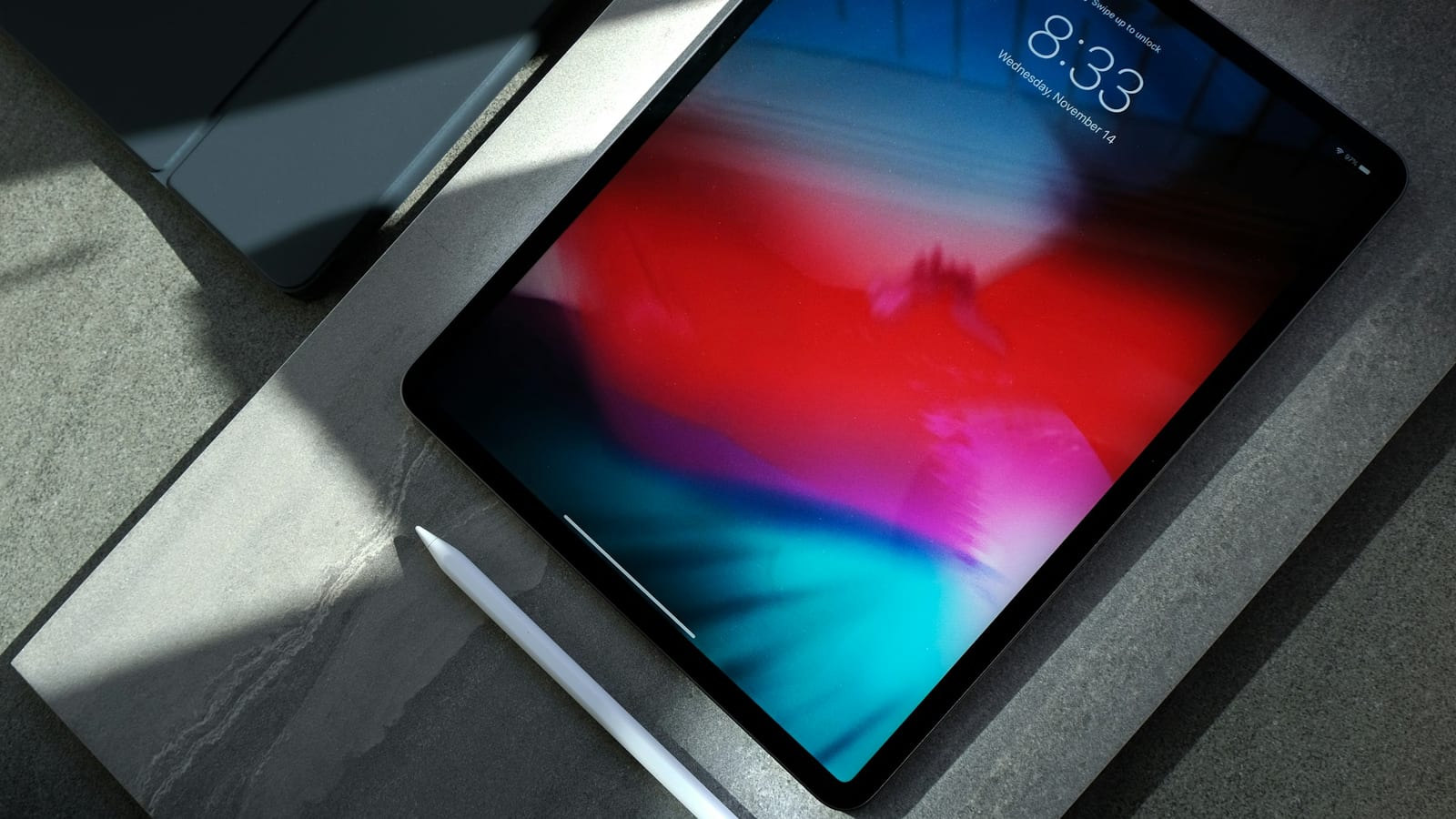 iPad Pro med färgstark låsskärm liggande på ett stenbord bredvid en Apple Pencil.