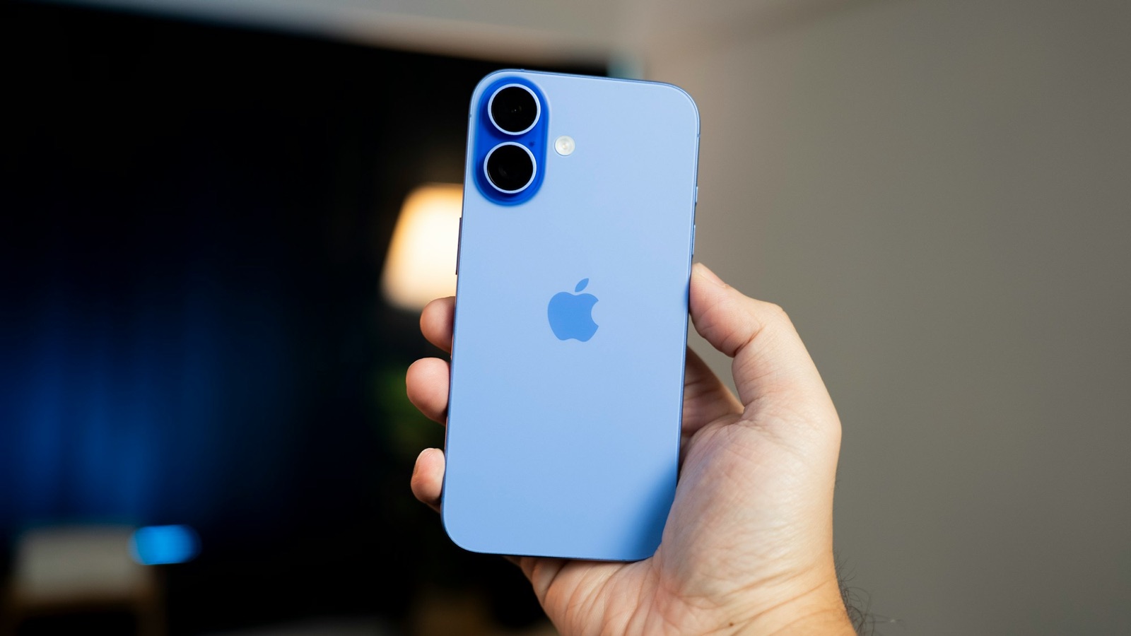 En ultramarinblå iPhone 16 med dubbla kameror, hållen i en hand