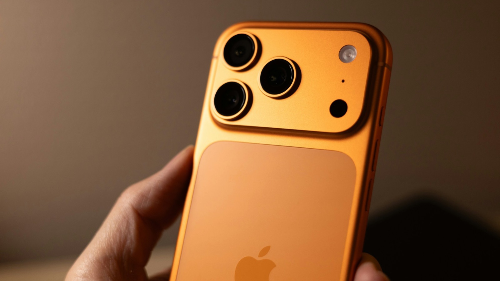 Baksidan av en iPhone 17 Pro i kosmiskt orange med tre kameror, hållen i en hand