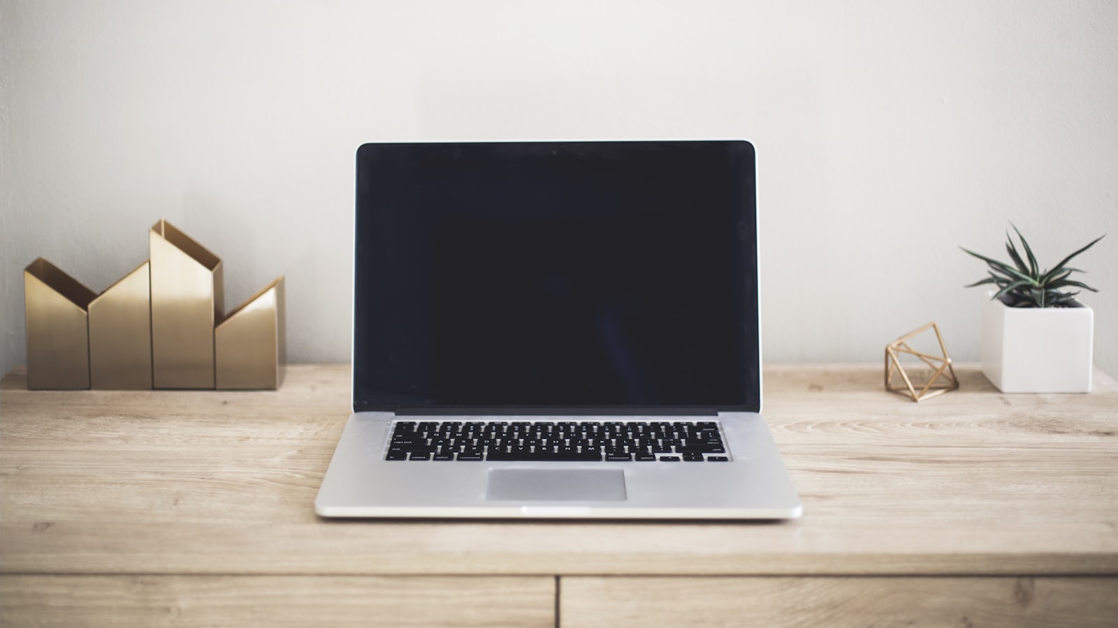 En öppen MacBook Pro på ett träskrivbord mot en ljus vägg